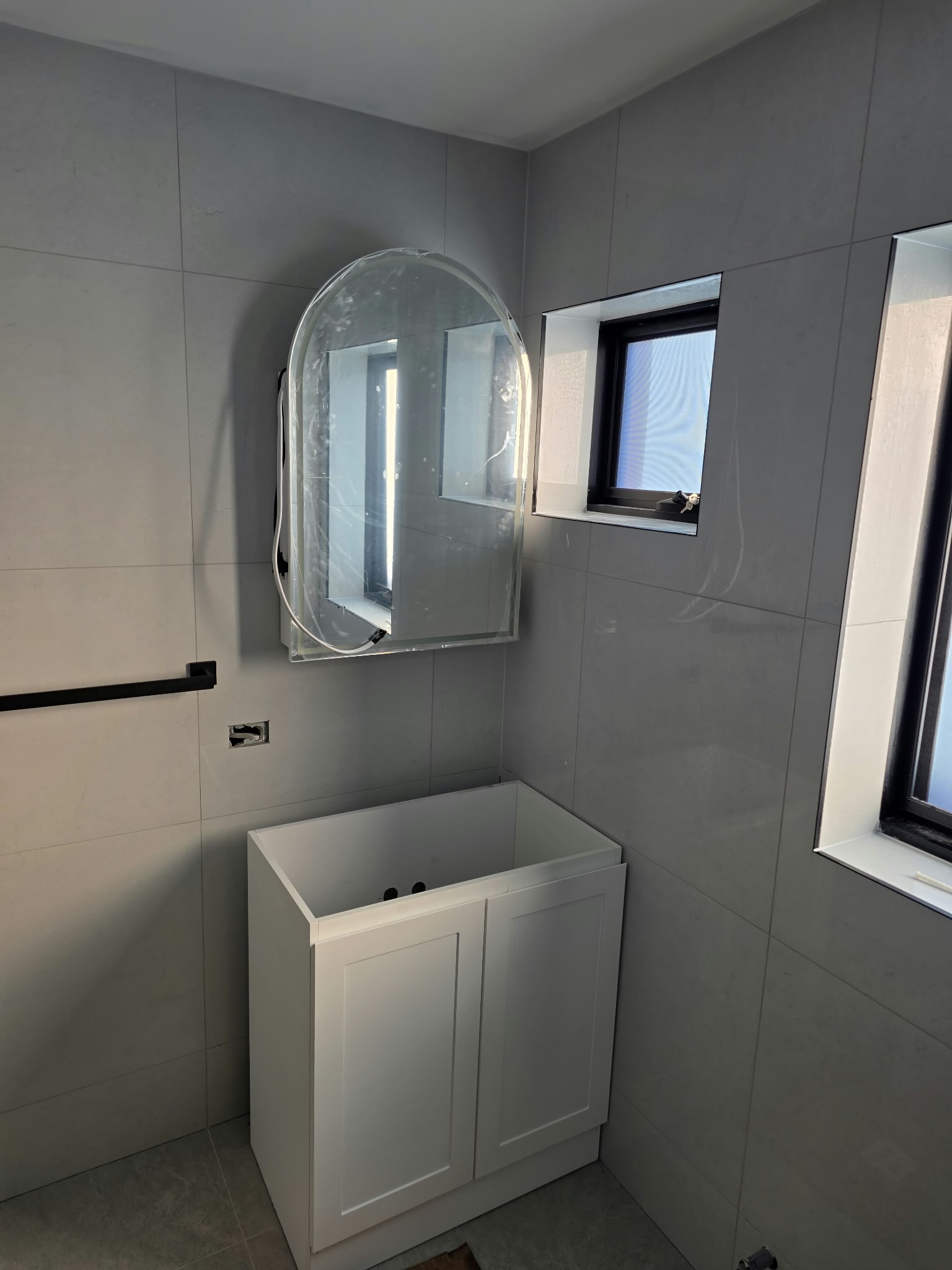 Renovated bathroom with large-format grey tiling, arched LED mirror and shaker vanity