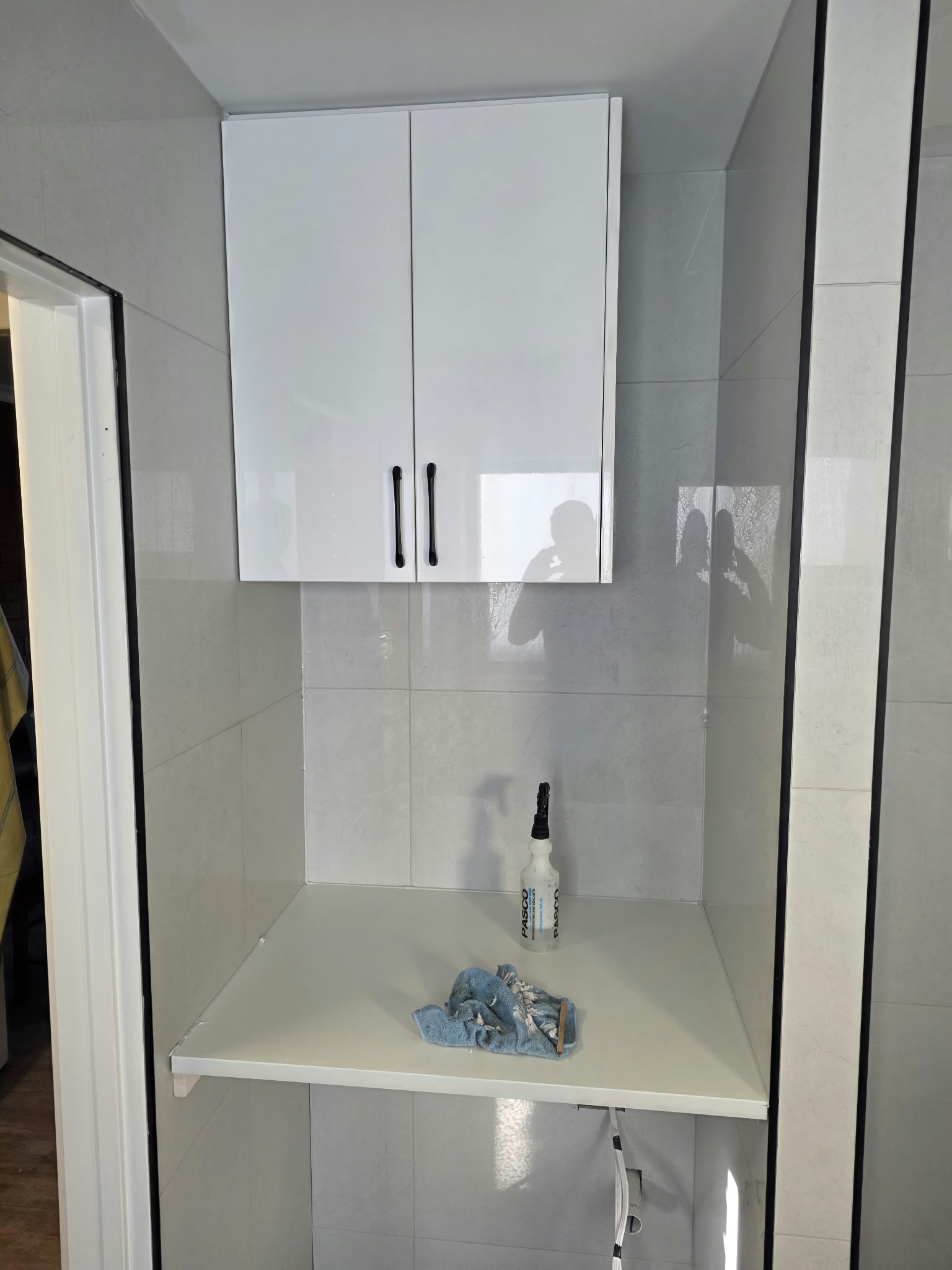 Renovated laundry with white tiling, overhead cabinet and a new benchtop