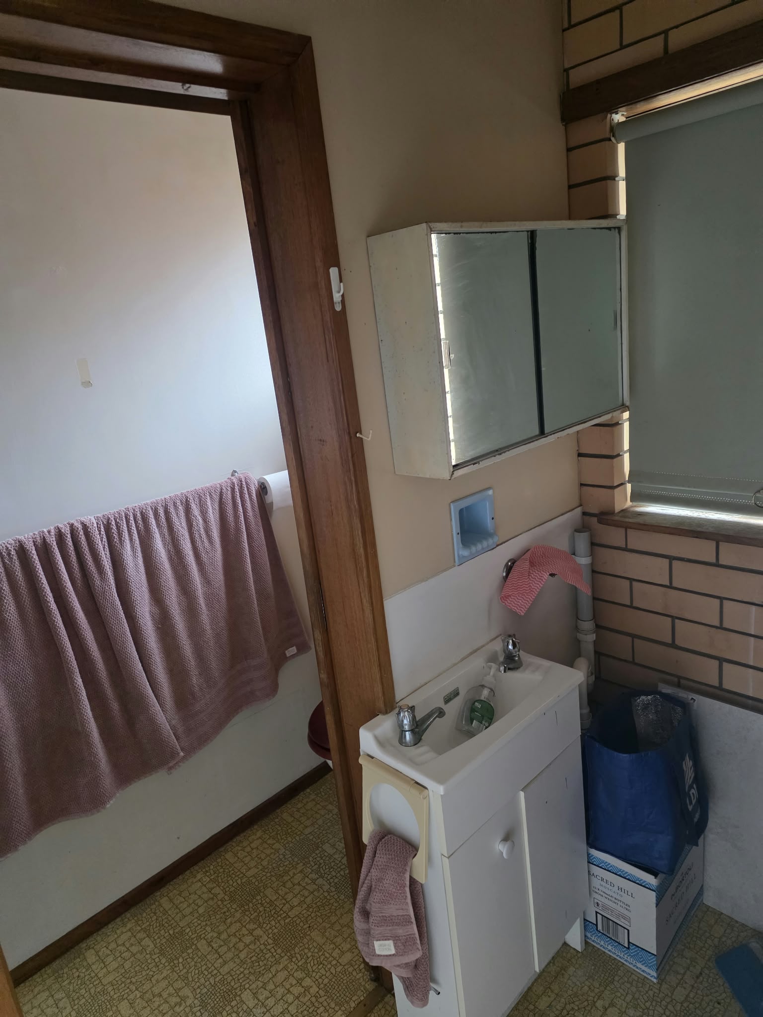 Bathroom before renovation, with beige brick tiles, a small basin and a mirrored cabinet