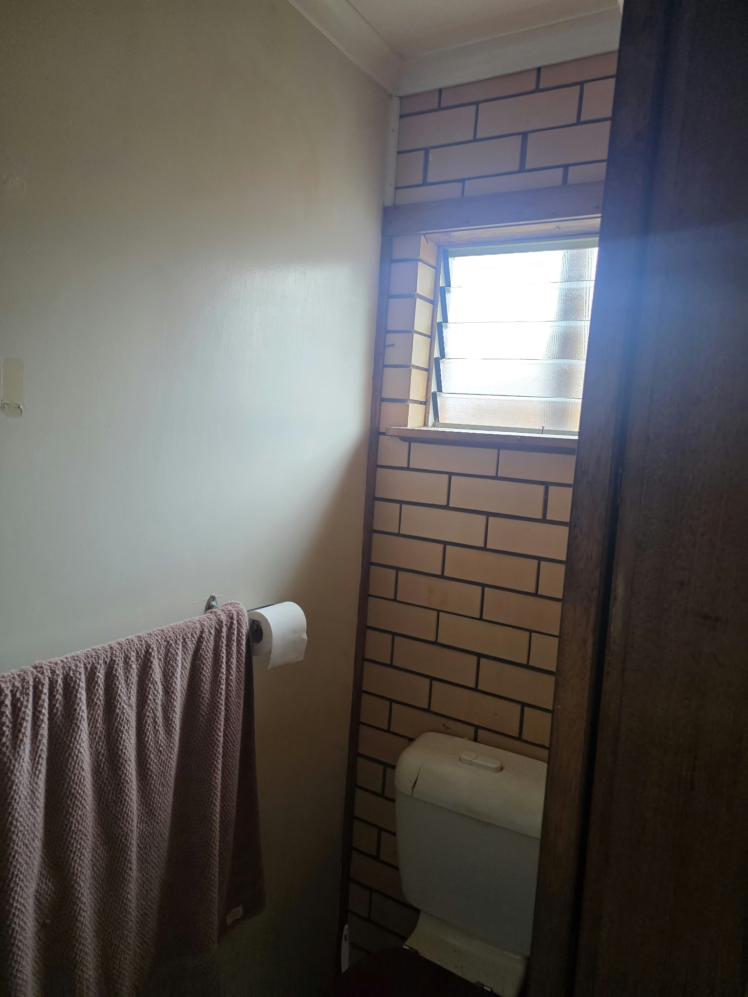 Separate toilet before renovation, with beige brick tiling and a louvre window