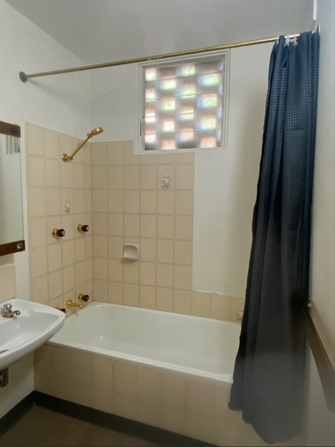 Original bathroom with cream tiling, a bath and brass tapware